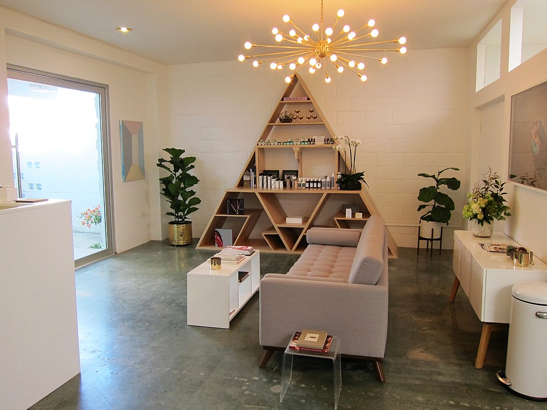 A design-forward beauty studio lounge with a triangular display shelf and a brass sputnik chandelier.
