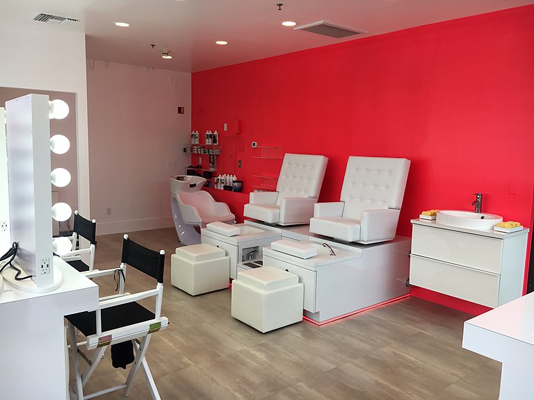 A beauty studio pedicure suite with white spa chairs against a bold red accent wall.