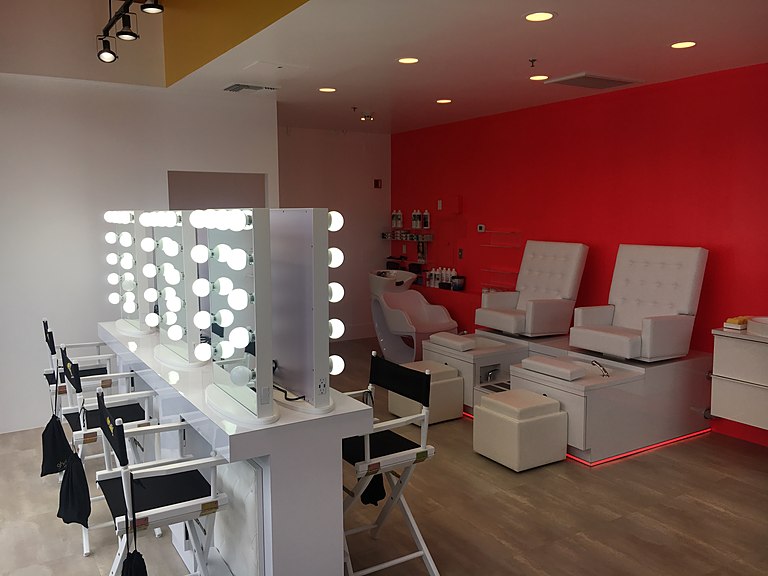 A beauty studio with backlit Hollywood makeup stations and white pedicure chairs against a red wall.